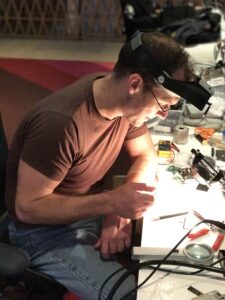 Engineer Dave Hayden at a desk, with welder's goggles pushed up on his head, working on Playdate 