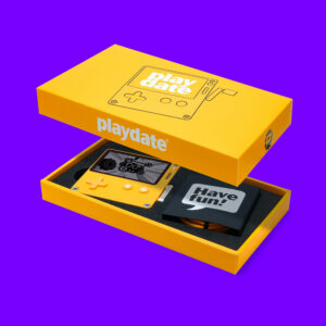 An image of Playdate in its box with the lid hovering above, so you can see the top of the box and how Playdate is packed inside. A card covering the USB-C cord reads, "have fun!" in a speech bubble.